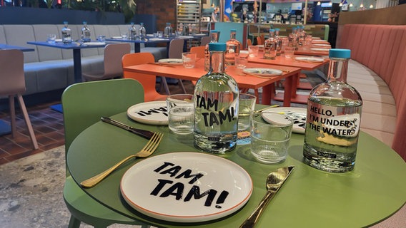 Teller und Flaschen mit der Beschriftung "Tam Tam" auf einem gedeckten Tisch. © NDR Foto: Karolin Weiß