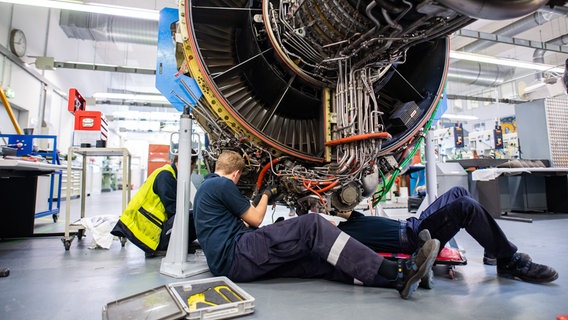 Drei Männer arbeiten in einer Werkstatt von Lufthansa Technik am Triebwerk eines Flugzeuges. © picture alliance/dpa Foto: Daniel Reinhard