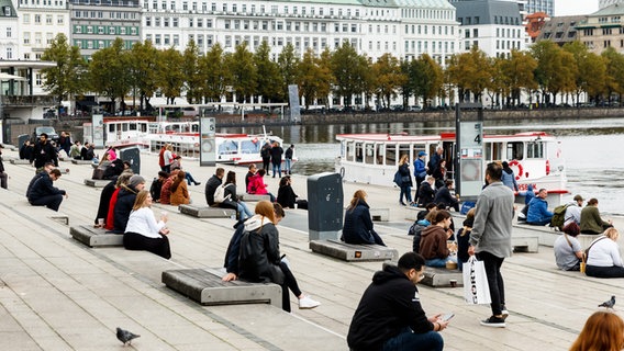 Bei bedecktem Himmel sitzen Menschen am Alsteranleger in Hamburg. © picture alliance/dpa | Markus Scholz Foto: Markus Scholz