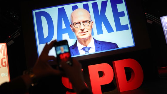 Eine Person fotografiert mit dem Smartphone eine Videowand mit dem Schriftzug "Danke" und dem Gesicht von Peter Tschentscher (SPD) bei der Wahlparty der Hamburger SPD in der Markthalle. © picture alliance/dpa | Christian Charisius Foto: Christian Charisius