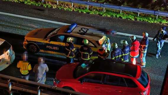 Mehrere Menschen stehen nach einem Unfall auf der Autobahn 25 in Hamburg neben einem Polizeiauto. © HamburgNews 