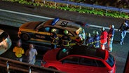 Mehrere Menschen stehen nach einem Unfall auf der Autobahn 25 in Hamburg neben einem Polizeiauto. © HamburgNews 