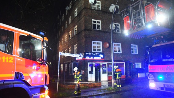 Zwei Einsatzwagen und zwei Feuerwehrmänner stehen in der Nacht zum Sonntag vor einem Eckhaus im Hamburger Stadtteil Veddel. © HamburgNews Verkauf 