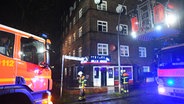 Zwei Einsatzwagen und zwei Feuerwehrmänner stehen in der Nacht zum Sonntag vor einem Eckhaus im Hamburger Stadtteil Veddel. © HamburgNews Verkauf 