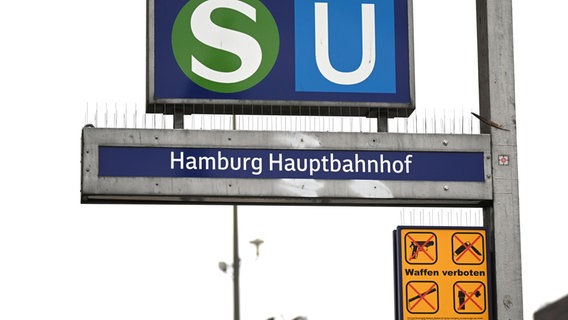 Ein gelbes Schild, das auf das geltende Waffenverbot hinweist, hängt unter dem Eingangsschild am Hamburger Hauptbahnhof neben den Logos von S-Bahn und U-Bahn. © Niklas Graeber/dpa Foto: Niklas Graeber