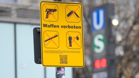 Ein gelbes Schild, das auf das geltende Waffenverbot hinweist, hängt unter dem Eingangsschild am Hamburger Hauptbahnhof neben den Logos von S-Bahn und U-Bahn. © picture alliance/dpa | Daniel Reinhardt Foto: Daniel Reinhardt