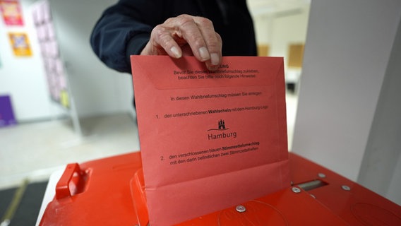 Ein Wähler steckt die Stimmzettel nach seiner Wahlabgabe in eine Wahlurne in der zentralen Briefwahlstelle zur Bürgerschaftswahl und Bundestagswahl 2025 auf dem Gerhart-Hauptmann-Platz. © picture alliance/dpa Foto: Marcus Brandt