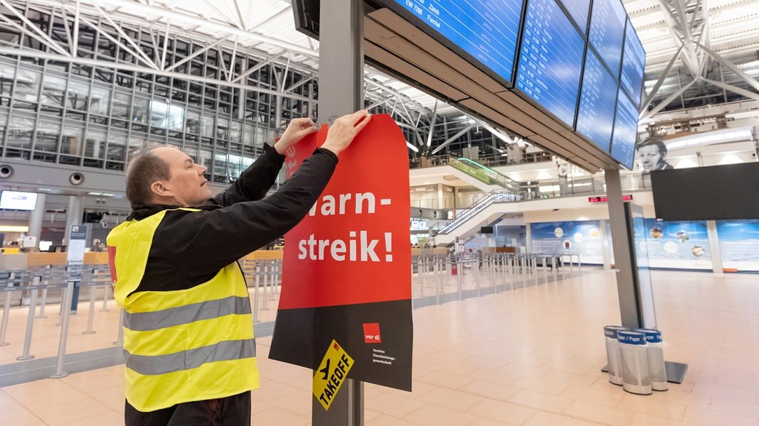 Ein Verdi-Vertreter hängt ein Plakat mit der Aufschrift «Warnstreik» in einem Terminal im Hamburger Flughafen auf.