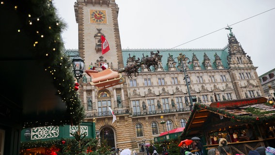 Ein Weihnachtsmann im fliegenden Renntierschlitten hängt an einem Seil beim Hamburger Weihnachtsmarkt auf dem Rathausmarkt. (Archivbild) © Christian Charisius/dpa Foto: Christian Charisius