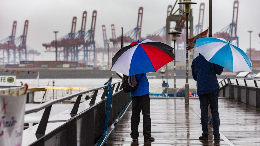 Bei Dauerregen gehen Spaziergänger durch den Museumshafen Oevelgönne in Hamburg.