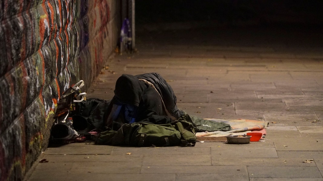 Ein Obdachloser liegt mit seinen Habseligkeiten auf dem Gehweg bei Minusgraden.