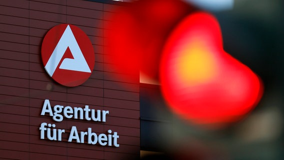 Eine rote Ampel ist neben dem Logo der Agentur für Arbeit zu sehen. © IMAGO / Panama Pictures 