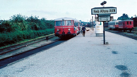 Ein Bahnsteig, an dem zwei rote Züge stehen. Personen steigen aus dem Zug aus. Auf einem Schild steht: Hmb: Altona AKN. © AKN Eisenbahn AG 