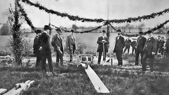 Einige Herren stehen auf einer Wiese. Es sind Richtfestsgirlanden zu sehen. Das Foto ist schwarz-weiß und wurde ca. Mitte des 20. Jahrhunderts aufgenommen. © AKN Eisenbahn AG 