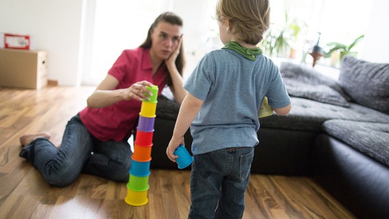 Eine alleinerziehende Mutter spielt mit ihrem Sohn im Wohnzimmer. © dpa 