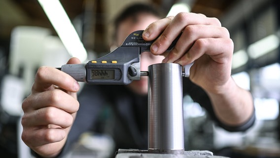 Ein Auszubildender im Metall-Handwerk misst in einem Ausbildungszentrum die Dicke eines Werkstücks. © dpa Foto: Felix Kästle