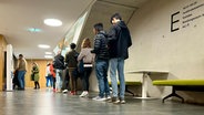 In der Ausländerbehörde in Wismar stehen Menschen auf einem Flur in einer Warteschlange. © NDR Info Foto: Anna-Lou Beckmann