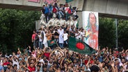 Demonstranten klettern auf ein öffentliches Denkmal und feiern, nachdem sie die Nachricht vom Rücktritt von Premierministerin Scheich Hasina erhalten haben. © Rajib Dhar/AP/dpa 