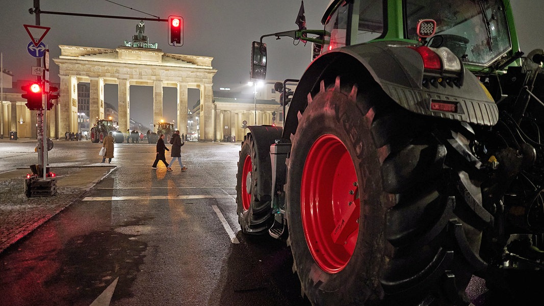 Ein Traktor steht im Dunklen in Berlin in der Nähe des erleuchteten Brandenburger Tors auf einer Straße.