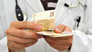 Mann im Arztkittel zählt Geldscheine © dpa - Bildfunk Foto: Tobias Hase