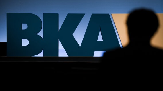 Ein Teilnehmer der BKA-Herbsttagung ist von hinten vor dem BKA-Logo der Behörde zu sehen. © picture alliance/dpa | Silas Stein 