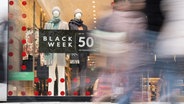 Werbung für den "Black Week Sale" hängt in einem Schaufenster, an dem Passanten vorbeigehen © picture alliance/dpa Foto: Etienne Dötsch