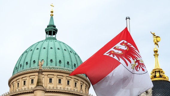 Die Landesflagge mit dem roten Brandenburger Adler weht vor der Kulisse der Nikolaikirche und der goldenen Fortuna im Hof des Brandenburger Landtages. © Soeren Stache/dpa Foto: Soeren Stache