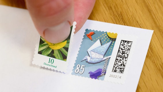 Eine 10-Cent-Briefmarke wird neben eine 85-Cent-Briefmarke geklebt (gestellte Szene). © dpa-Bildfunk Foto: Julian Stratenschulte/dpa