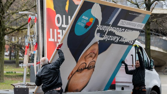 Arbeiter laden ein Wahlplakat, das den Vorsitzenden der CDU, Merz, zeigt, auf einen Lieferwagen neben einem Plakat, das Bundeskanzler Scholz (SPD) zeigt. © Rolf Vennenbernd/dpa Foto: Rolf Vennenbernd