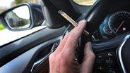 Ein Mann sitzt mit einem Joint zwischen den Fingern am Steuer eines Autos. © picture alliance/dpa Foto: Karl-Josef Hildenbrand