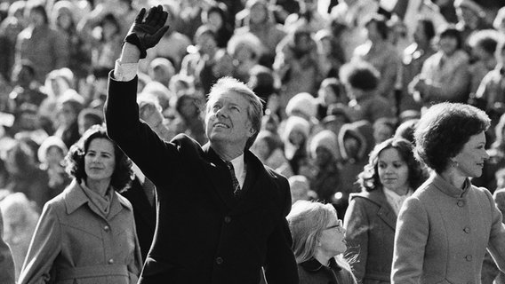 Präsident Jimmy Carter winkt der Menge zu, während er nach seiner Amtseinführung am 20. Januar 1977 in Washington mit seiner Frau Rosalynn und seiner Tochter Amy die Pennsylvania Avenue vom Kapitol zum Weißen Haus entlanggeht. © Suzanne Vlamis/AP/dpa 