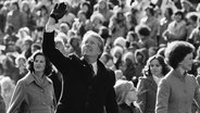 Präsident Jimmy Carter winkt der Menge zu, während er nach seiner Amtseinführung am 20. Januar 1977 in Washington mit seiner Frau Rosalynn und seiner Tochter Amy die Pennsylvania Avenue vom Kapitol zum Weißen Haus entlanggeht. © Suzanne Vlamis/AP/dpa 