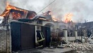 Ein Feuerwehrmann steht vor einem brennenden Haus im ukrainischen Cherson, das nach ukrainischen Angaben bei russischem Beschuss am orthodoxen Weihnachtsabend getroffen wurde. © Libkos/AP/dpa 