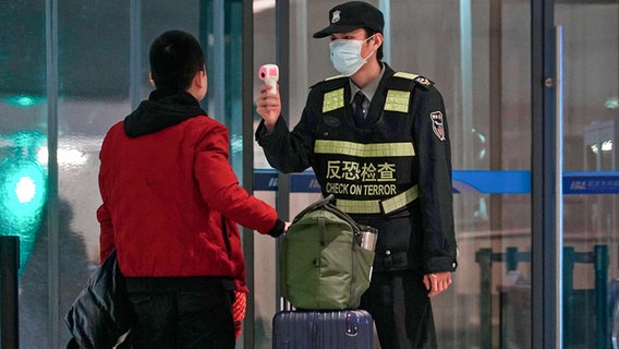 Ein Mitarbeiter des Flughafen Wuhan Tianhe International Airport trägt Mundschutz und misst bei einem Reisenden Temperatur. © dpa bildfunk/AP Foto: Dake Kang