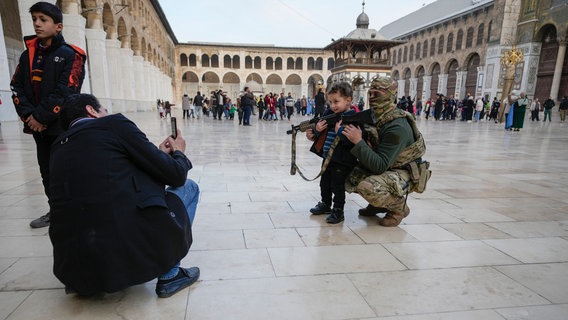 Kind posiert in der syrischen Hauptstadt Damaskus für ein Foto mit einem Kämpfer von Hayat Tahrir al-Sham (HTS) © Hussein Malla/AP/dpa Foto: Hussein Malla/AP/dpa