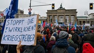 Teilnehmer einer Friedensdemonstration verschiedener Initiativen auf dem Platz des 18. März in Berlin halten unter anderem ein Plakat mit der Aufschrift "Stoppt die wirklichen Kriegstreiber". © picture alliance/dpa | Soeren Stache 