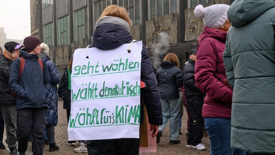 Während einer Demonstration gegen rechts in Bremen trägt eine Teilnehmerin ein Plakat auf dem Rücken mit der Aufschrift: "Geht wählen, wählt demokratisch, wählt fürs Klima". © Izabela Mittwollen/dpa 