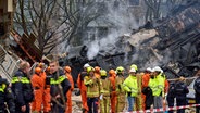 Feuerwehrleute stehen in Den Haag in den Niederlanden vor einem zerstörten Gebäude am Ort einer Explosion, bei der mehrere Wohnungen zerstört und mehrere Menschen verletzt wurden. © picture alliance/dpa/AP Foto: Phil Nijhuis