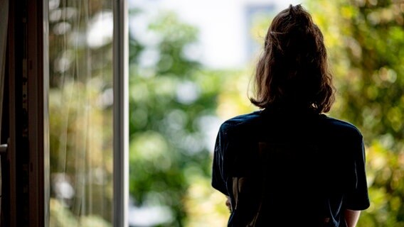 Eine Frau steht in ihrer Wohnung an einem Fenster. (Symbolbild Depression) © Fabian Sommer/dpa 