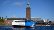 Die elektrische Tragflächenfähre Nova bewegt sich während eines Tests, mit dem Stockholmer Rathaus im Hintergrund, in Stockholm. © dpa-Bildfunk Foto: Henrik Montgomery/TT News Agency/AP/dpa