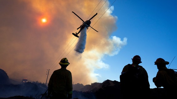 Ein Hubschrauber wirft auf den Hügel hinter Pacific Palisades im Topanga State Park Löschwasser ab, um die Flammen zu bekämpfen. © dpa bildfunk/ZUMA Press Wire Foto: Daniel A. Anderson