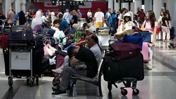In einer Halle des Flughafens von Beirut im Libanon sitzen viele Passagiere mit Gepäck und warten. © Hussein Malla/AP/dpa Foto: Hussein Malla