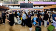 In einer Halle des Flughafen BER stehen und gehen zahlreiche Reisende mit Gepäck. © dpa Foto: Christoph Soeder