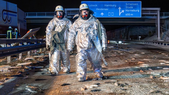 Feuerwehrleute in Schutzanzügen gehen nach einem LKW-Unfall auf der Autobahn zwischen toten Forellen über die Fahrbahn © JOTO/dpa 