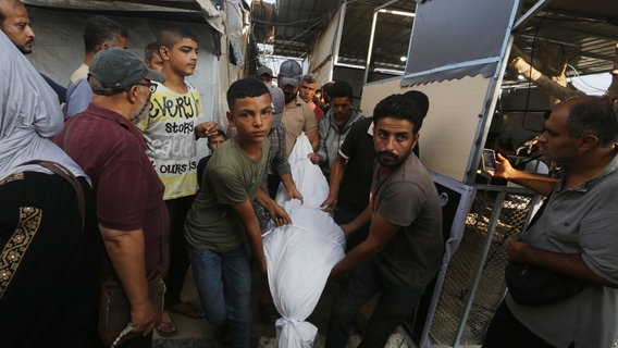 Menschen im Gazastreifen tragen eine ein Tücher gehüllte Leiche nach einem Angriff Israels © Omar Ashtawy/APA Images via ZUMA Press Wire/dpa Foto: Omar Ashtawy