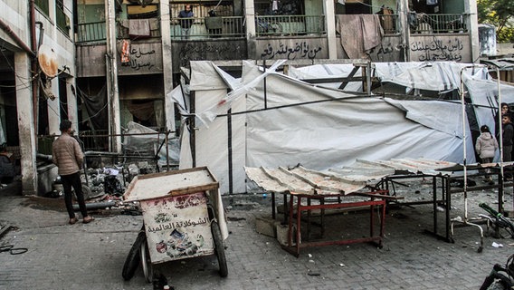 Mehrere Menschen begutachten die Schäden in einem ehemaligen Schulgebäude im Gazastreifen, in dem Flüchtlinge untergebracht waren. © dpa picture alliance/ZUMAPRESS Foto: Mahmoud Issa