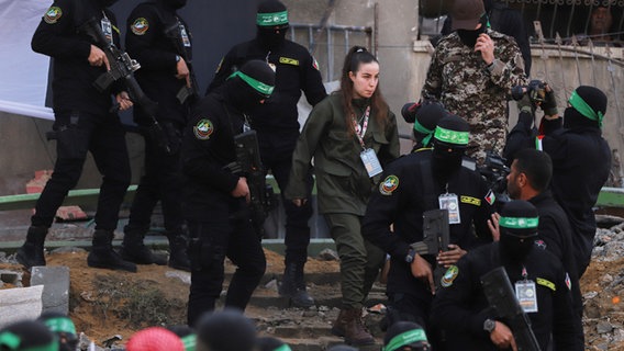 Die israelische Soldatin Agam Berger geht neben maskierten Kämpfern des Islamischen Dschihad, als sie im Flüchtlingslager Dschabalija in Gaza-Stadt dem Roten Kreuz übergeben wird. © dpa-Bildfunk Foto: Mohammed Hajjar/AP/dpa