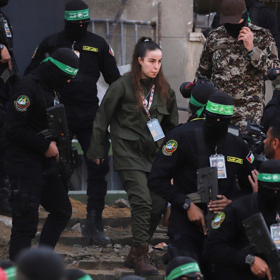 Die israelische Soldatin Agam Berger geht neben maskierten Kämpfern des Islamischen Dschihad, als sie im Flüchtlingslager Dschabalija in Gaza-Stadt dem Roten Kreuz übergeben wird. © dpa-Bildfunk Foto: Mohammed Hajjar/AP/dpa