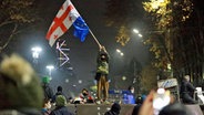 Ein Demonstrant steht mit georgischen National- und EU-Flaggen während einer Kundgebung vor dem Parlamentsgebäude in Tiflis, um gegen die Entscheidung der Regierung zu protestieren, die Verhandlungen über den Beitritt zur Europäischen Union für vier Jahre auszusetzen. © Zurab Tsertsvadze/AP/dpa 