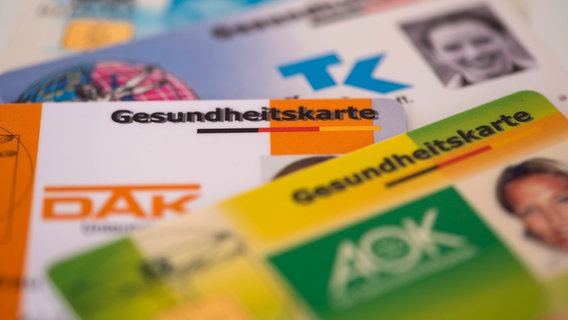 Gesundheitskarten verschiedener Krankenkassen liegen zusammen. © IMAGO / Wolfilser 